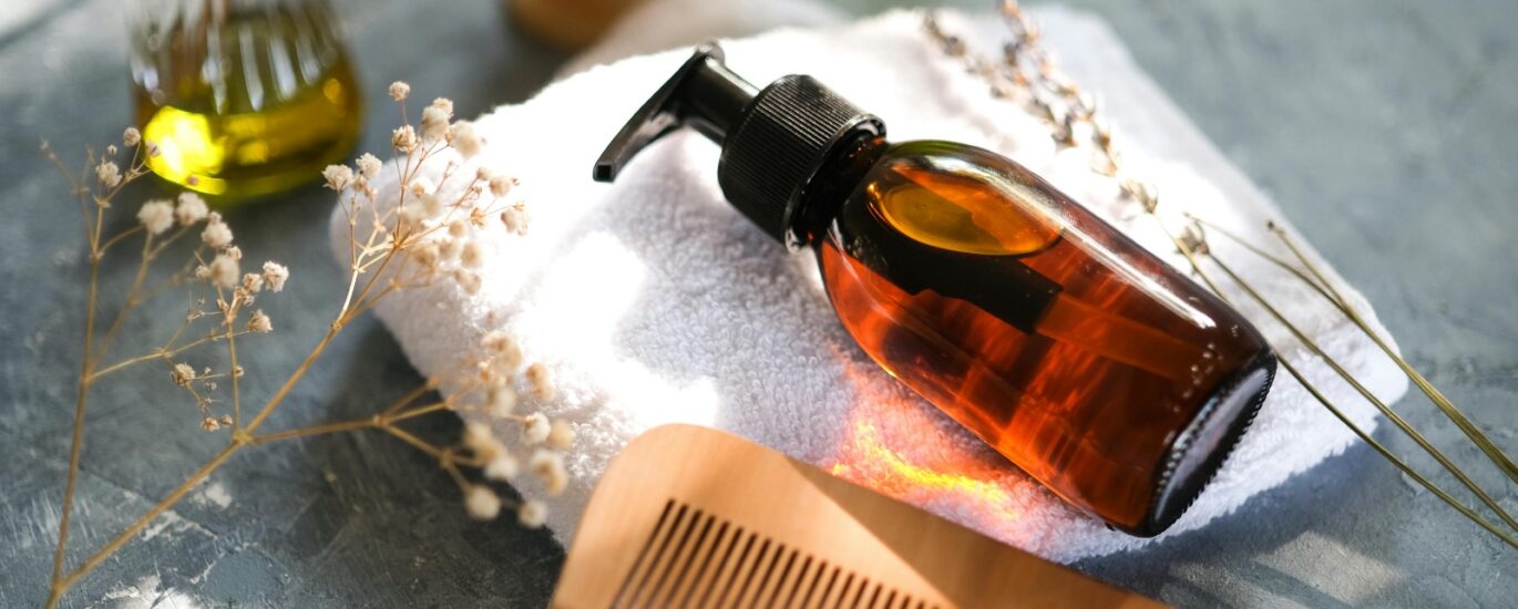 Natural hair oil bottle with wooden comb on towel.
