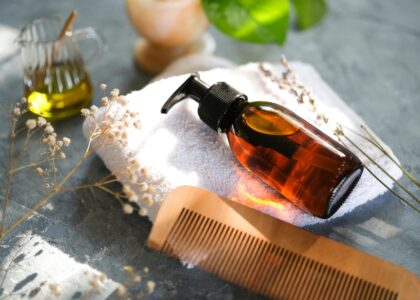 Natural hair oil bottle with wooden comb on towel.